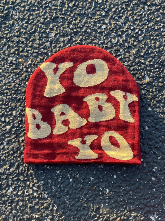 Red beanie with 'YO BABY YO' text on a textured black surface